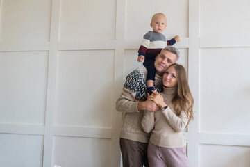 Happy young family with toddler son on grey apartment wall background with copy space. Rental, moving, mortgage concept
