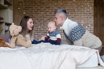 Affectionate young family having fun playing with little son on bed at home. Happy parenthood concept