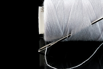 A spool of white thread and a needle