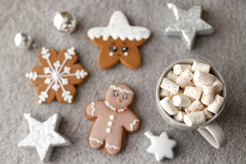 Flat lay set of ginger and cinnamon cookies: gingerbread man, snowflakes, stars decorated with icing and with cup of hot chocolate with marshmallow on grey background with xmas toys. 