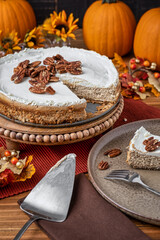 Slice of homemade pumpkin cheesecake served on a plate with a scatter of pecans to top it off. - 473140695