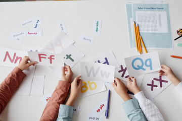 Close-up of children sitting at the table together with cards and learning English alphabet © Seventyfour