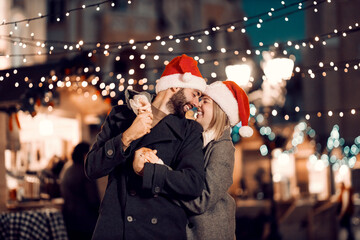 Romantic Christmas couple cuddling on the street on Christmas eve. A happy laughing couple with Santa hats on their heads is standing on the street on Christmas eve hugging and cuddling.