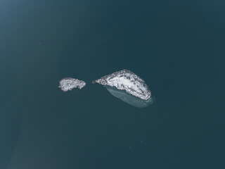 Tiny icy , snowy island in the blue water lake from above. Small iceberg floating abstract.