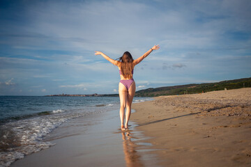 Happy beautiful woman walking on the beach on sunlight.