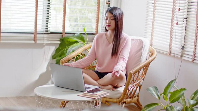 Beautiful Asian woman meditation with yoga after work or take a break to relax her mind and body.Calm of Young woman yoga Exercise lotus pose deep breath sit on chair at cozy home.Meditation Concept