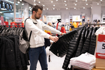 Adult handsome brunet man chooses warm jacket in a clothing store in a shopping mall. Outerwear and shopping