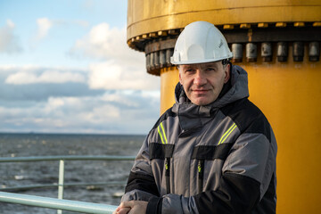 A professional in overalls. Shift worker of the Arctic oil platform. On his head is the white helmet of the master.