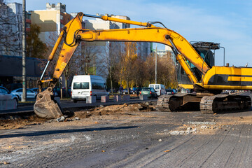 An excavator in a modern city is carrying out work during the reconstruction of the road. Repairs in the city with heavy construction equipment.