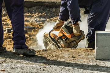 A construction worker cuts a road curb with a gas saw. Road surface repair. Installation of a curb stone.