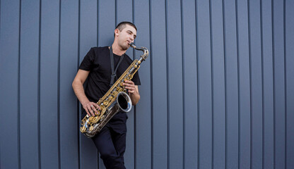 Young street musician playing saxophone near the big blue wall