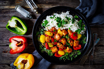 Fried chicken nuggets with white rice, bell peppers and parsley on wooden table