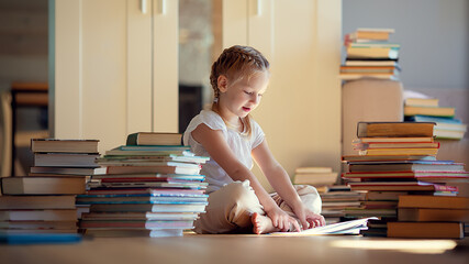 A little cute girl in a yellow dress reading a book sitting on the floor.