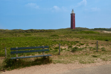 Fototapeta na wymiar Red lighthouse at Ouddorp, green pastureland and bench, blue sky. Ouddorp, Netherlands.