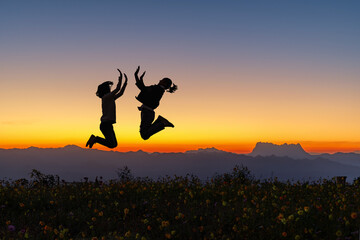 Silhouette of happy jumping teenager girlfriend on flowers mountain at colorful sunset sky...