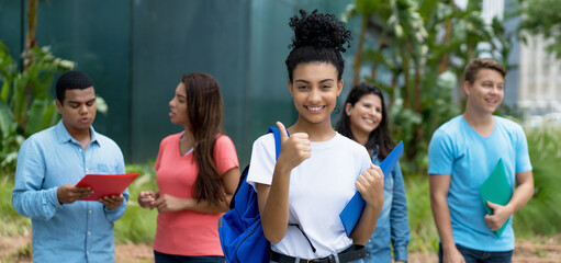 Happy indian female student showing thumb up with group of multi ethnic young adults