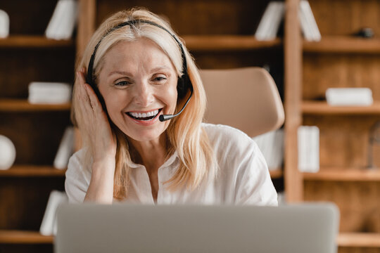 E-learning, teaching tutoring concept. Mature middle-aged hotline worker, IT support agent, secretary wearing headset while talking helping clients using laptop in office.
