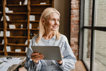 Smiling caucasian businesswoman freelancer ceo tutor leader teacher using digital tablet for e-banking, remote work, watching webinars, social media, e-learning online in home office.