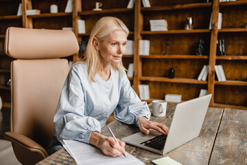 Caucasian mature businesswoman signing documents, contracts, doing paperwork while working on...