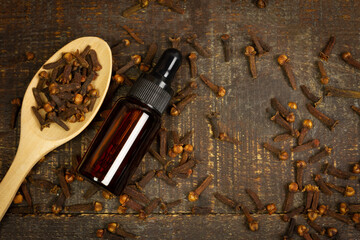 Fototapeta na wymiar Essential oil of cloves in bottle and dry cloves on wooden spoon on rustic wooden background, top view.