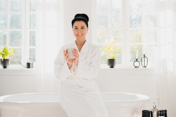 Morning breakfast. Beautiful caucasian woman in white spa bathrobe drinking hot beverage coffee tea while relaxing after beauty bath procedures at home hotel resort.