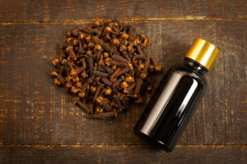 Essential oil of cloves in bottle and dry cloves on rustic wooden background, top view.