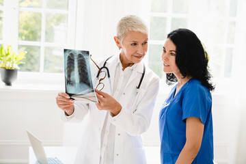 Caucasian senior female doctor showing x-ray image of lungs to medical student intern nurse...