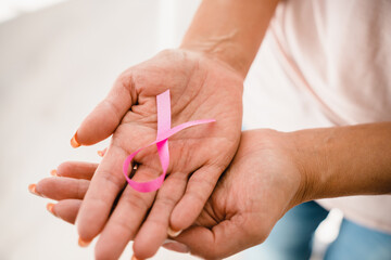 Close up cropped shot of women`s hands holding pink ribbon in support of breast cancer. World...