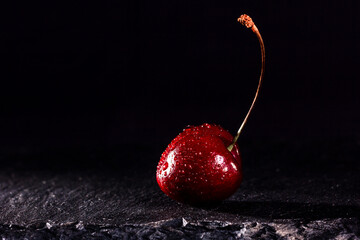 one red cherry with water drops on black stone background