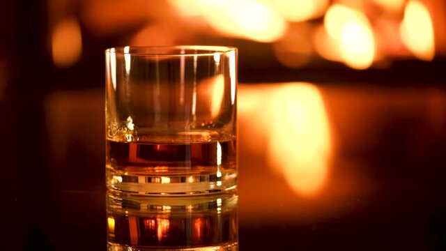One glass with whiskey on the fireplace background. 
