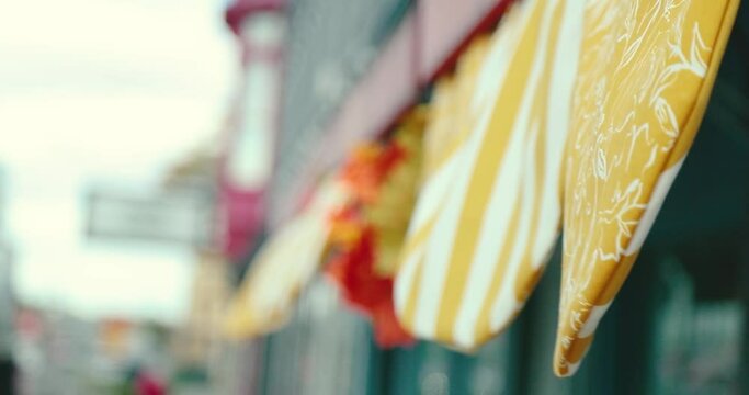 Yellow decorative fabric hanging off the awning of a small business in a quaint little town. Wind blows the pattern printed flags in the air. Shot in 4k slow motion.