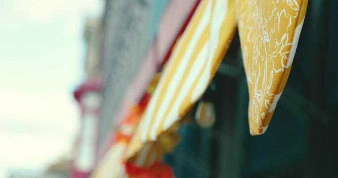 Yellow decorative fabric hanging off the awning of a small business in a quaint little town. Wind blows the pattern printed flags in the air. Shot in 4k slow motion.