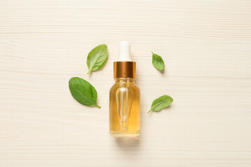Bottle of essential basil oil and fresh leaves on white wooden table, flat lay