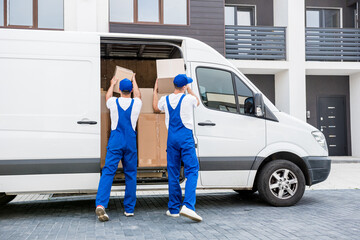 Two removal company workers unloading boxes from minibus into new home