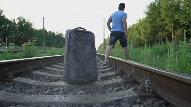 adult male traveler put road bag on railway and went into grass to urinate outdoors on summer day