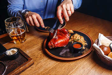 A man cuts a pork knuckle with a knife and fork with stewed cabbage on a plate.