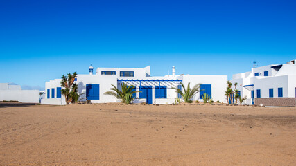 Typical canarian white and blue houses in Caleta del Sebo town on la Graciosa island, near Lanzarote in Spain. Beautiful traditional home on deserted sandy terrain near sea under bright blue sky