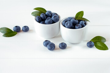 fresh blueberries in white bowls on a white background. background with fresh ripe blueberries and green leaves.