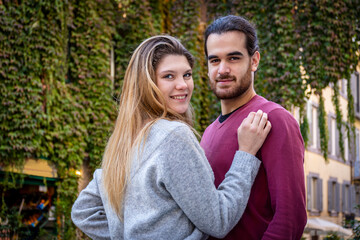 Young couple traveling to Rome. Beautiful blonde woman hugs her boyfriend. In the background, a street in the historic center with an ivy-covered building.