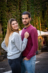 Obraz premium Young couple traveling to Rome. Beautiful blonde woman hugs her boyfriend. In the background, a street in the historic center with an ivy-covered building.