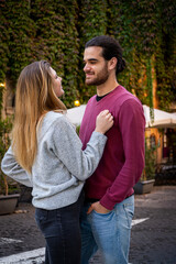 Obraz premium Young couple traveling to Rome. The beautiful blonde woman hugs her boyfriend and looks into her eyes. In the background a street in the historic center with a building covered with ivy. Love concept.