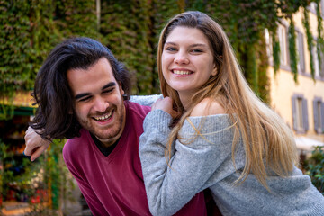Obraz premium Young couple traveling to Rome. The beautiful blonde woman hugs her boyfriend and smiles. In the background a street in the historic center with a building covered with ivy. Love concept.