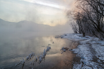 Winter landscape, river with icy banks, mountains in the fog.