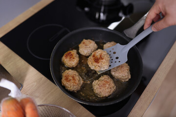 Meat balls beginning to fry in oil in frying pan on kitchen stove