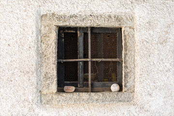 Vecchia finestra quadrata, chiusa e sbarrata, su facciata di casa con antico muro di colore bianco. Tipico particolare del paese di Topolo (Topolove) nelle valli del fiume Natisone in Friuli.