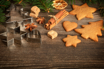 Ginger cookies, cinnamon, citrus, anise, bakeware and green Christmas tree branches on dark rustic wooden background