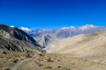 Photo sur Plexiglas Dhaulagiri A pathway leading through dry Himalayan slopes, in Mustang region, Annapurna Circuit Trek in Nepal. In the back there is snow capped Dhaulagiri I. Barren and steep slopes. Harsh landscape.