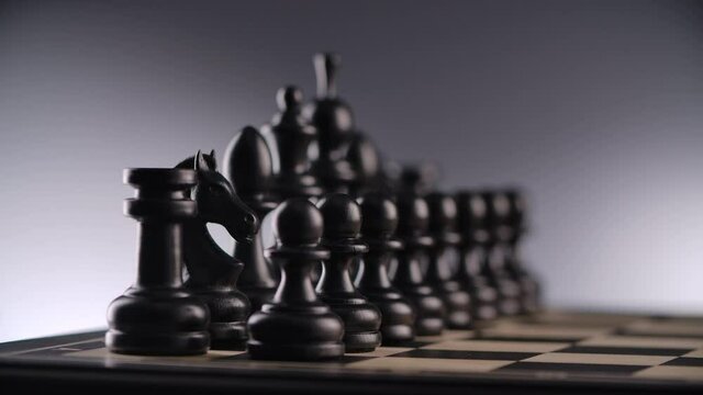 Close-up of wood chessboard with lines of black wooden chess figures in a row ready to play with blurred background. Slider move. 4K