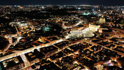 Aerial drone night shot of iconic masterpiece Saint Peter Basilica and whole illuminated city of Vatican the biggest church in the world, Metropolitan city of Rome, Italy