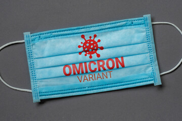 A blue medical face mask lies on a dark grey background with the inscription omicron variant, coronavirus concept